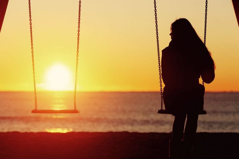 donna sull'altalena in riva al mare al tramonto